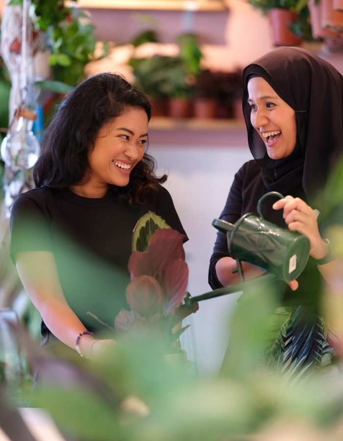 Two people holding a plant and a watering can